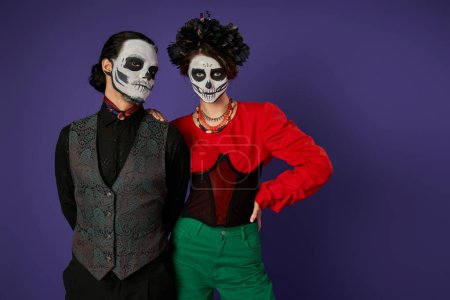 Téléchargez les photos : Couple élégant dans le maquillage squelette traditionnel dia de los muertos regardant la caméra sur fond bleu - en image libre de droit