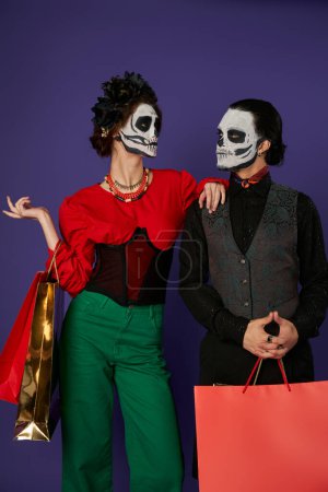 dia de los muertos couple in catrina makeup holding shopping bags and looking at each other on blue
