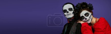 Photo for Woman in catrina calavera makeup and black wreath leaning on shoulder of eerie man on blue, banner - Royalty Free Image