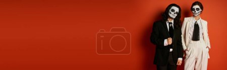 Téléchargez les photos : Couple à la mode dans dia de los muertos crâne de sucre maquillage et costumes regardant caméra sur rouge, bannière - en image libre de droit