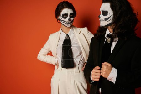 woman in skeleton makeup and white suit looking at spooky man on red, dia de lost muertos tradition