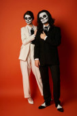 full length of couple in dia de los muertos skull makeup and festive suits looking at camera on red puzzle #676493226