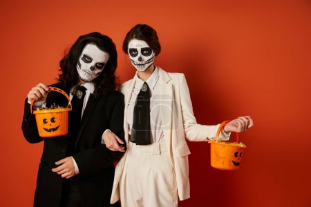 elegant couple in dia de los muertos makeup holding candy buckets and looking at camera on red