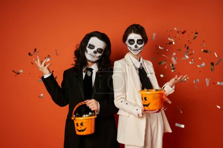 pareja en catrina maquillaje lanzando confeti brillante de baldes de caramelo en rojo, fiesta de día de los muertos