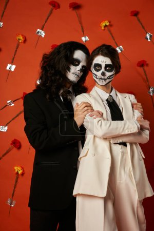 dia de los muertos couple, woman with folded arms near spooky man on red backdrop with carnations tote bag #676494852