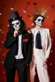 couple in scary skeleton makeup and festive attire on red backdrop with flowers, dia de los muertos Stickers #676495760
