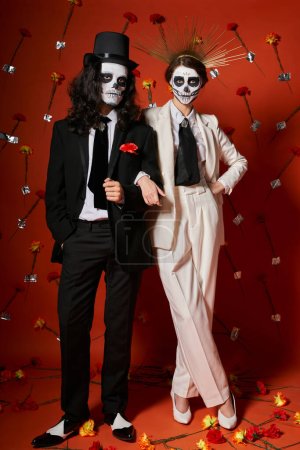 Foto de Larga duración de pareja elegante festiva en día de los muertos maquillaje sobre fondo rojo con decoración floral - Imagen libre de derechos