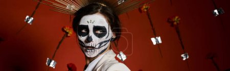 Photo for Scary woman in dia de los muertos sugar skull makeup looking away on red floral backdrop, banner - Royalty Free Image