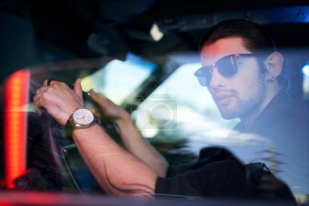 joven atractivo posando detrás del volante de su coche con reloj de pulsera, conductor sexy