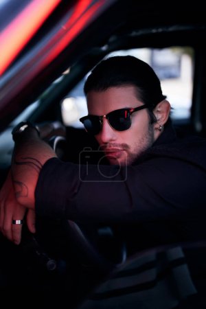 tiro vertical de hombre sexy en traje negro con los brazos cruzados en el volante mirando a la cámara