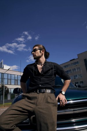 vertikale Aufnahme eines stilvollen sexy Mannes mit Sonnenbrille und Armbanduhr, der in der Nähe von Auto posiert und wegschaut