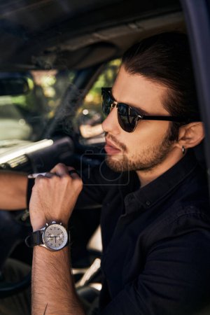 gut aussehender junger Mann mit Sonnenbrille und Armbanduhr sitzt in seinem Auto und posiert im Profil