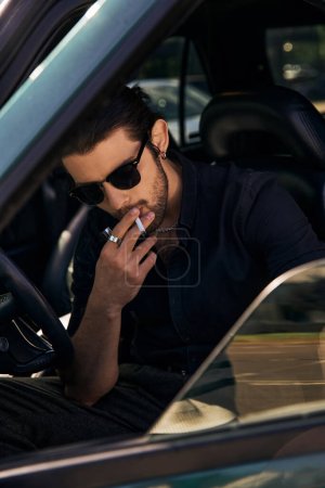 vertical shot of appealing sexy man posing with cigarette behind driving steering wheel, style