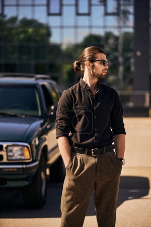 Blickfang junger Mann mit Accessoires posiert neben seinem Auto mit den Händen in den Taschen, sexy Fahrerin