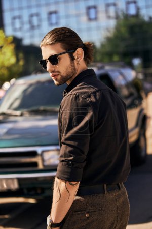 vertical shot of eye catching man with ponytail and accessories posing near his car, sexy driver