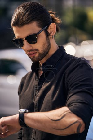 vertikale Aufnahme eines gut aussehenden männlichen Modells im eleganten schwarzen Outfit mit Blick auf seine Armbanduhr, Mode