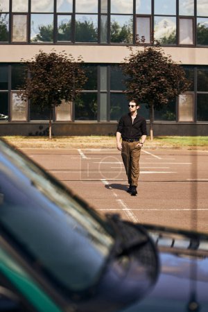 schöner junger Mann in schwarzer trendiger Kleidung, der mit der Hand in der Tasche zu seinem Auto geht, Modekonzept