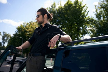 attraktive sexy Fahrer posiert im Profil neben seinem Auto und schaut weg, Modekonzept