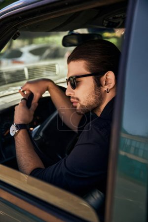 modische junge männliche Modell mit schickem Blick sitzt hinter dem Lenkrad seines Autos, sexy Fahrer