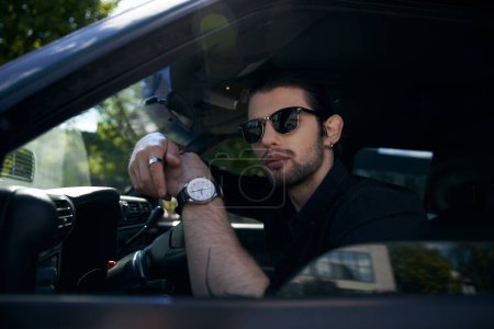 handsome sexy driver in black outfit behind steering wheel and looking at camera, fashion concept