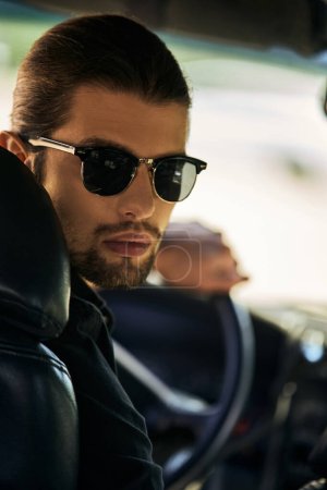Photo for Vertical shot of appealing young man with sunglasses behind steering wheel and looking at camera - Royalty Free Image