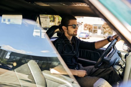 handsome young man with accessories in black shirt sitting behind steering wheel, sexy driver