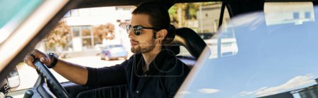 Photo for Appealing young man with accessories in black shirt behind steering wheel, sexy driver, banner - Royalty Free Image