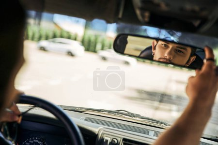 atractivo joven detrás del volante de su coche y mirando en el espejo retrovisor, conductor sexy