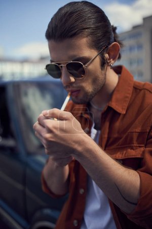 retrato de un hombre joven y elegante con gafas de sol iluminando su cigarrillo, vertical, concepto de estilo