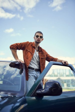 Foto de Tiro vertical de joven atractivo en ropa vibrante elegante posando al lado de su coche, la moda - Imagen libre de derechos