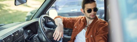 jeune homme en chemise marron et jeans refroidissant dans sa voiture derrière le volant, chauffeur sexy, bannière