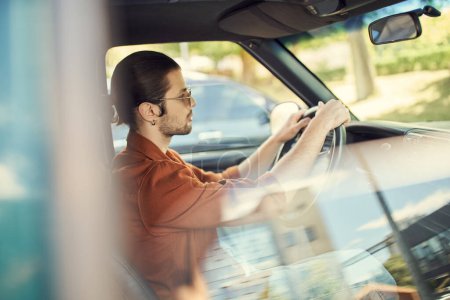 Foto de Hombre atractivo de buen aspecto en camisa marrón con gafas de sol y pendiente de conducir su coche, la moda y el estilo - Imagen libre de derechos