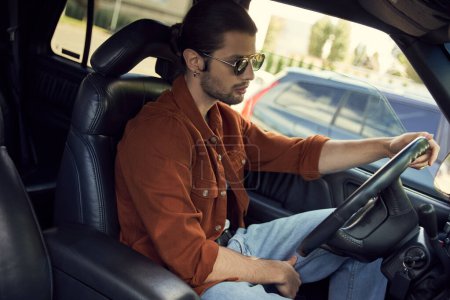 attraktive sexy Fahrer mit stylischer Brille in braunem Hemd hinter dem Lenkrad seines Autos, Mode