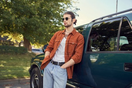 beau modèle masculin avec look dapper posant à côté de sa voiture avec les mains dans les poches, chauffeur sexy