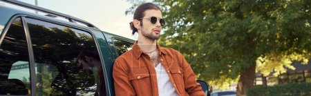 hombre sexy guapo en camisa marrón y jeans posando al lado de su coche, concepto de moda, bandera