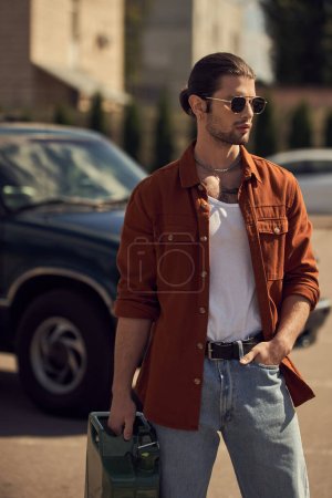 appealing sexy man with sunglasses and ponytail holding petrol canister with hand in pocket