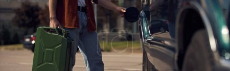 Foto de Vista recortada de un hombre joven en camisa marrón elegante con jeans repostando su coche con gasolina, pancarta - Imagen libre de derechos