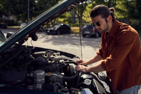 attractive stylish male model in trendy urban attire with accessories checking on his car engine