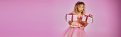 lovely blonde woman in tooth fairy costume showing presents on camera on pink backdrop, banner puzzle #676831888