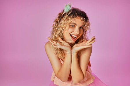 fröhliche attraktive Frau im rosafarbenen Kostüm der Zahnfee, die mit geschlossenen Händen in die Kamera lächelt