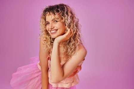 Foto de Primer plano de alegre mujer encantadora en traje rosa sonriendo sinceramente a la cámara con la mano levantada a la cara - Imagen libre de derechos