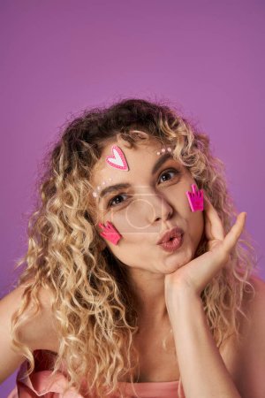 attractive blonde woman with curly hair and bright face stickers expressing astonishment at camera