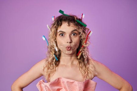 verblüffte blonde Frau in rosafarbenem Outfit und Zahnbürsten im Haar, Zahnfee-Konzept