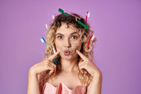 Photo for Joyous tooth fairy with toothbrushes in her hair pointing fingers at her cheeks looking at camera - Royalty Free Image