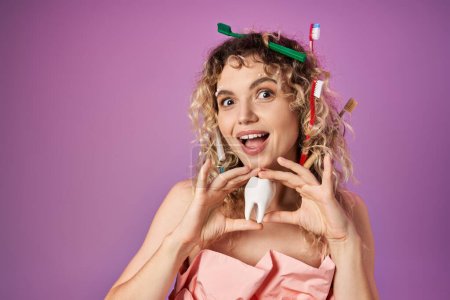 fröhliche Zahnfee im rosafarbenen Outfit mit Zahnbürsten im Haar, die Babyzahn in die Kamera halten