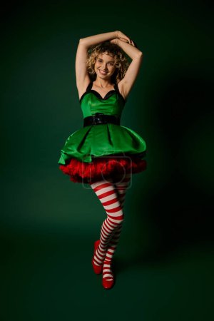mujer alegre vestida como elfo de año nuevo posando con el brazo levantado al pelo y sonriendo a la cámara