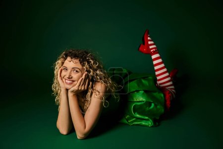 jolly new year elf in green dress and striped stockings with leg slightly raised smiling at camera