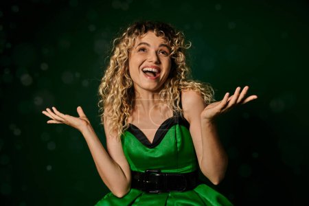 Photo for Cheerful woman in new year elf costume looking at snow and catching snowflakes on green background - Royalty Free Image