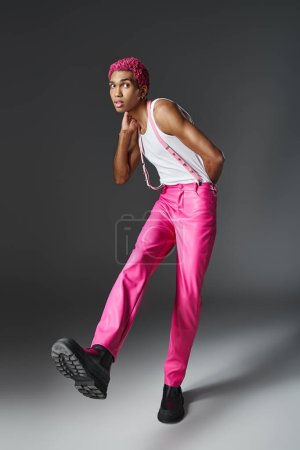 élégant homme aux cheveux roses en pantalon rose avec bretelles et bottes noires avec lacets, mode et style