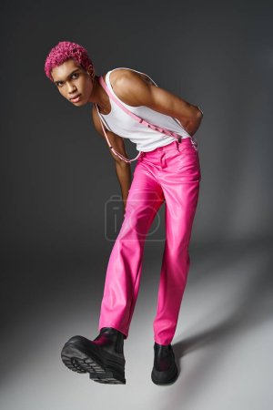 modèle masculin afro-américain élégant avec cheveux bouclés roses regardant la caméra, la mode et le style